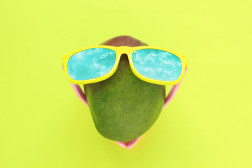 Ripe juicy green and red mango in sunglasses on pastel yellow background.Copy space. minimalistic style.