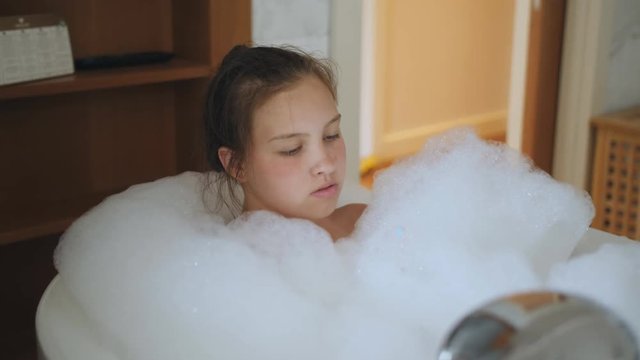 A teenage girl in the bathtub full of foam relaxes.