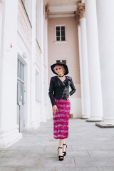 Young pretty positive sexy caucasian girl walking in the street in sexy dress and stylish black hat with pink hair smiling and having a nice day. Beauty,success, education concept