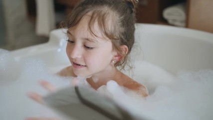 Little girl playing with shower attachment while taking the bath. Happy child girl in the shower. Positive little girl having bath with bubbles in bathtub - Powered by Adobe
