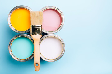 Brush with wooden handle on open cans on blue pastel background. Yellow, white, pink, turquoise...