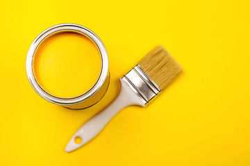 One open can of paint with white brush on it on yellow background. Top view. Repairing concept.
