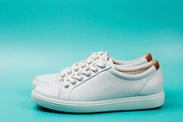 Side view of white trendy sneakers on turquoise background. Vertical photo.