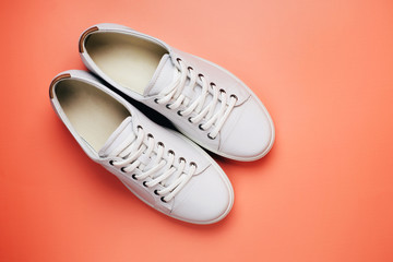 Toes of white trendy sneakers on bright orange background. Place for text.
