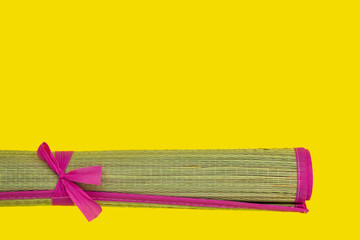 Wicker bast beach mat with pink edging rolled into roll on a yellow background. Hot summer and beach theme. Copy space.