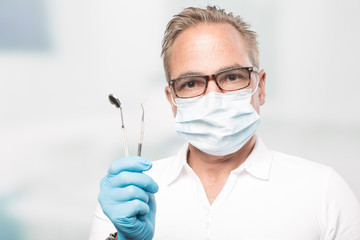 dentist with gloves and face mask holding a dental tool