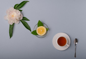 A cup of tea, fresh lemon and white peony on a light blue background.
