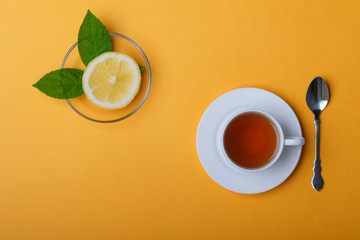 White cup of tea and fresh lemon on a yellow background.
