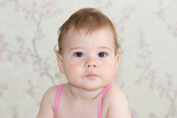 Cute little girl 10 months old, baby portrait close-up. The baby is looking at the camera with a serious face, baby girl with brown eyes, soft focus