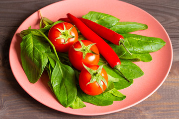 Ripe tomatoes, spinach and hot red pepper on a bamboo plate. Edible vegetables for cooking food, organic vegan vegetarian, bright red and green colors