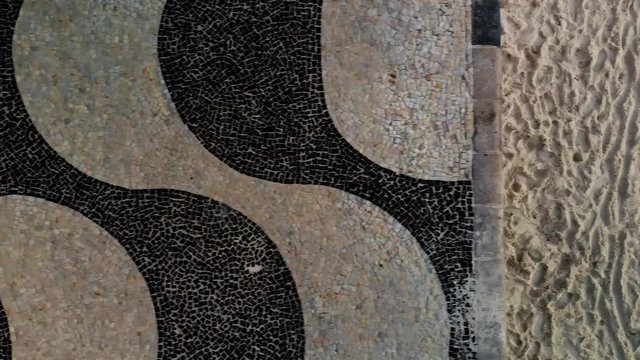 Top down aerial split view of Copacabana beach with patterns in the sand on the right and the pavement boulevard on the left. Slowed down from 60fps.