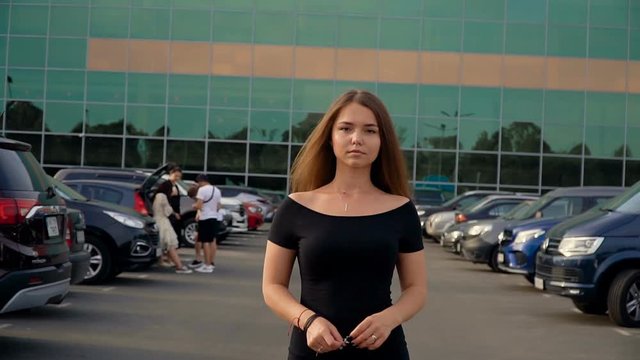 The camera follows a young attractive brunette in the parking lot.
