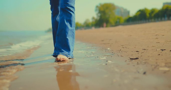 Woman walks along the bank of the river, her bare feet walking along the water. Rest by the sea. Close-up.