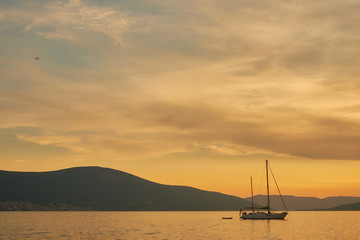 Fototapeta na wymiar yacht with a small boat in the sunset light on the background of mountains and a flying plane.