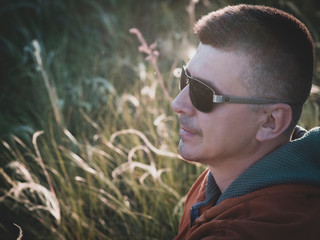 Man sitting in the background of nature. The man in sunglasses looks thoughtfully into the distance. Dreams and hopes of an adult in a close-up photo.