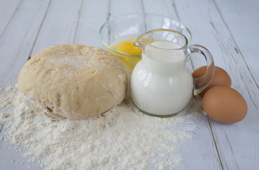 Still life of a jug of milk, flour and eggs on old white boards of a kitchen table