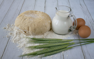 Still life of a jug of milk, flour, green ears of wheat and eggs on old white boards of a kitchen table
