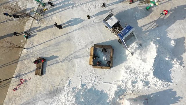Flying past heavy machinery loader shoveling snow towards sculpture under construction at Harbin ice festival in China