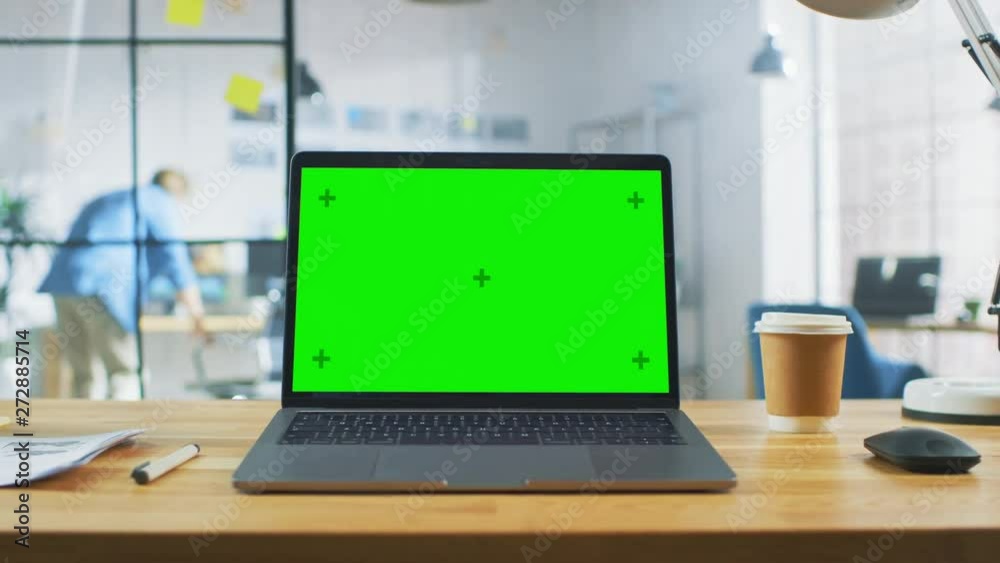 Poster laptop on the desk in the office shows green mock-up screen. in the background bright creative open 