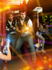 Fototapeta na wymiar Emotional guy playing laser tag in colorful beams