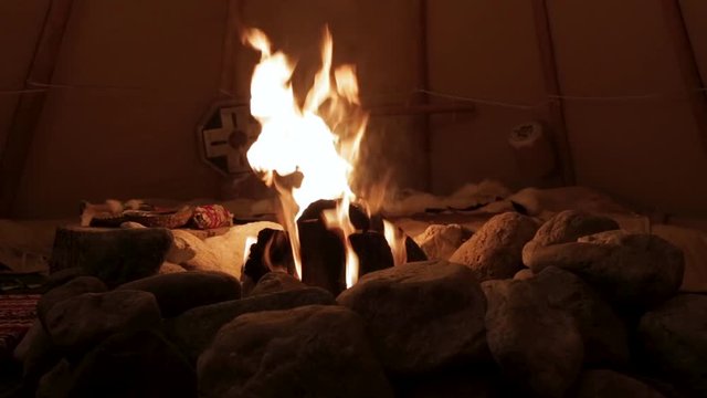 A steady shot of a beautiful cozy campfire from inside a Native American teepee