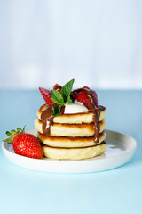 Syrniki served with sour cream, strawberry and melted chocolate. White plate, blue table, high resolution