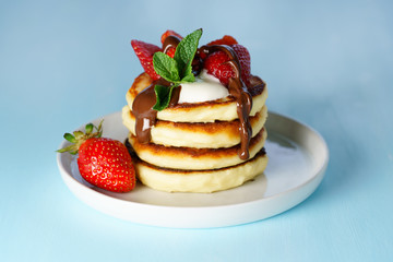 Syrniki served with sour cream, strawberry and melted chocolate. White plate, blue table, high resolution