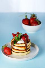 Syrniki served with sour cream, strawberry and melted chocolate. White plate, blue table, high resolution