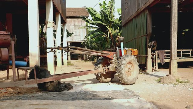 panning shot of a corn sheller machine next to stilt-houses in a farmyard