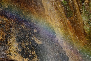 A rainbow is created in the mist and water droplets of a waterfall