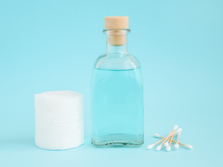 Tonic for face skin or makeup remover in a glass bottle, cotton pads and wooden cotton buds on pastel blue background. Hygiene supplies, beauty tools and skin care.