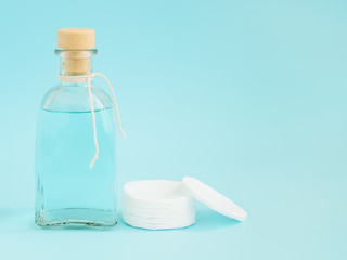 Tonic for face skin or makeup remover in a glass bottle and cotton pads on pastel blue background. Hygiene supplies, beauty tools and skin care. Copy space.