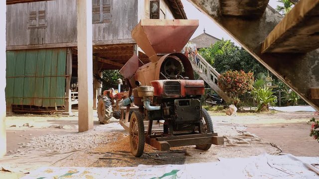 corn sheller machine next to stilt-houses in a farmyard