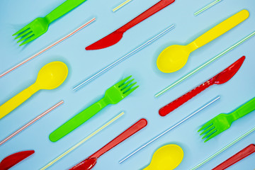 Multicolored plastic disposable tableware on light blue background.