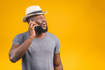Portrait of a happy travel african american guy talking on mobile phone isolated against yellow background.