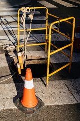 Street warning orange construction cone near manhole protected with yellow security fence