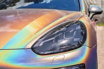 Close-up LED headlight expensive car part with exclusive iridescent painting. Vehicle covered with...