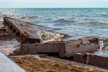 Destruction from the storm at sea. Broken concrete blocks of a building in the waves.