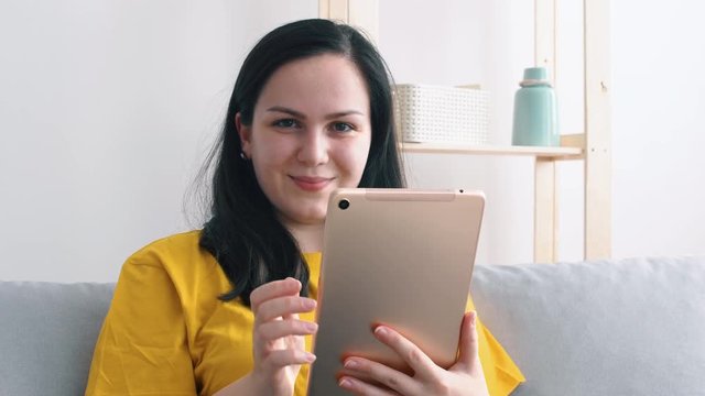 Portrait of a young beautiful woman in yellow t-shirt who uses a tablet.