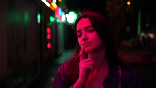 portrait of playful young woman on the street with pink neon signs late night. Close up