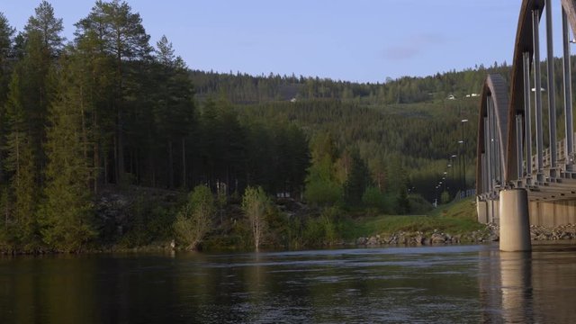 Pan shot to the right in the trysil river towards a tied arch bridge in Norway.