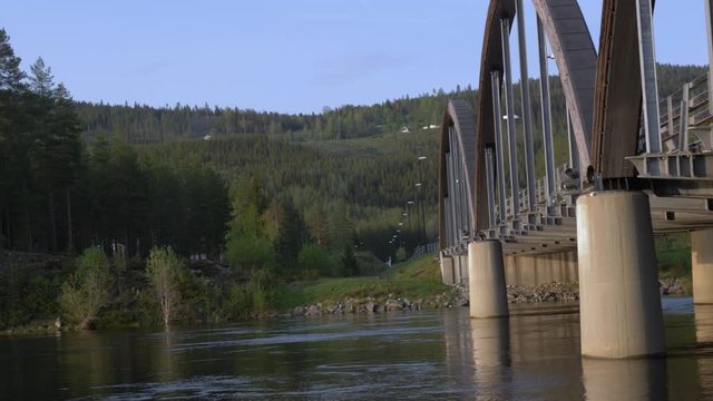 Pan shot to the left on the trysil river with a tied arch steel bridge and the river flowing slowly.