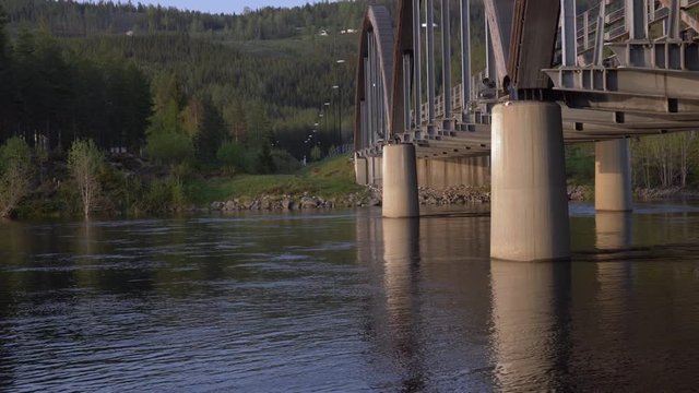 Tilt up shot of the trysil river flowing slowly under a tied arch bridge in Norwayl.