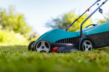 Electric lawn mower cuts moss and green grass. The alignment of the green lawn with the mower. Close-up in front of a green lawn mower on wheels on the background of the garden