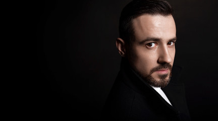 Handsome bearded man in a black coat. Black background, copy space.
