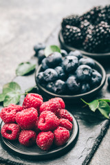 Fresh berries with raspberries, blueberries, blackberries in bowl on a stone stand on a dark metal background.