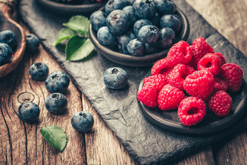 Fresh berries with raspberries, blueberries, blackberries in bowl on a stone stand on wood...