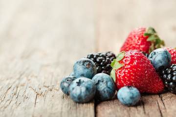 Fresh Summer Berries mix with Strawberry, Raspberry, Red currant, Blueberry and Blackberry on wood background.