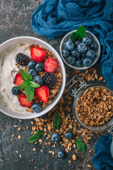 Healthy breakfast with granola, yogurt, fruits, berries on dark metal background. Summer homemade breakfast.