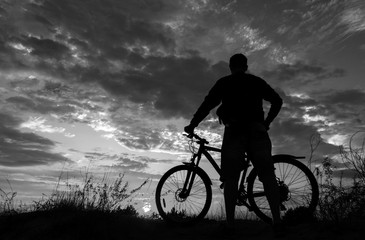 Obraz premium rowerzysta z rowerem, w tle ognisty zachód słońca.